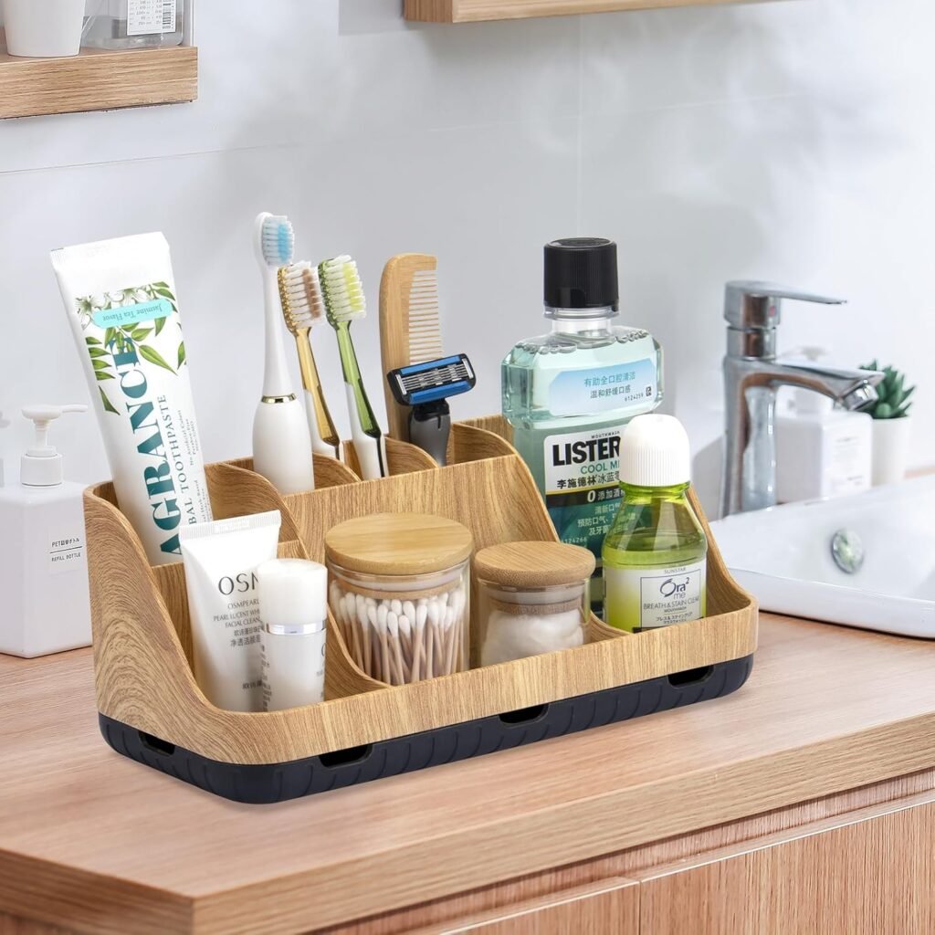 Wood and black bathroom countertop organizer holding toothbrushes, toothpaste, mouthwash, skincare bottles, a razor, and glass jars filled with cotton swabs and cotton pads, placed beside a modern sink.